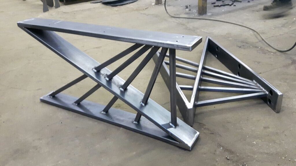 Металлические ножки для стола, выполненные с высокой точностью, лежат на полу мастерской.